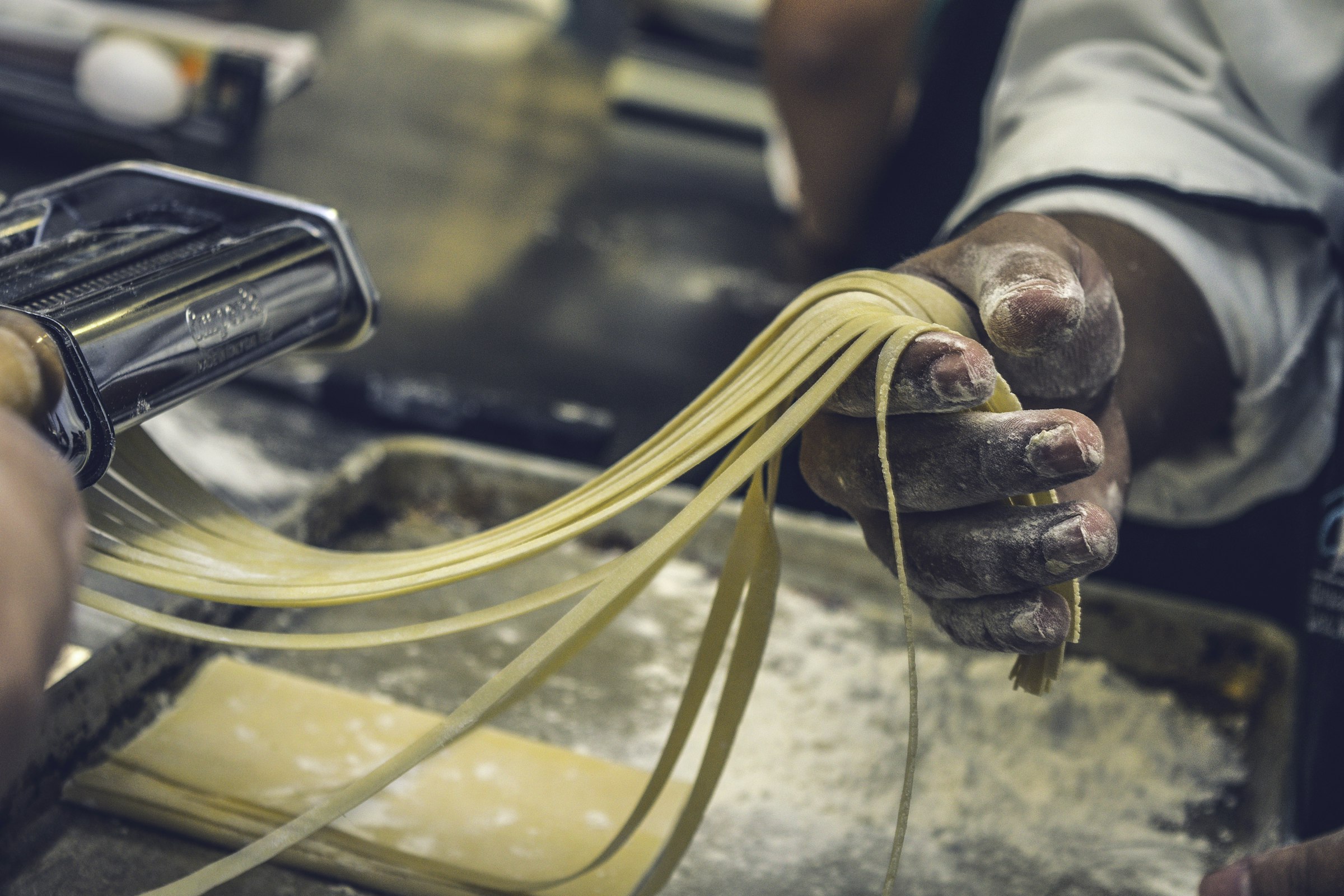 Mani infarinate stendono la sfoglia di pasta fresca alla sfogliatrice