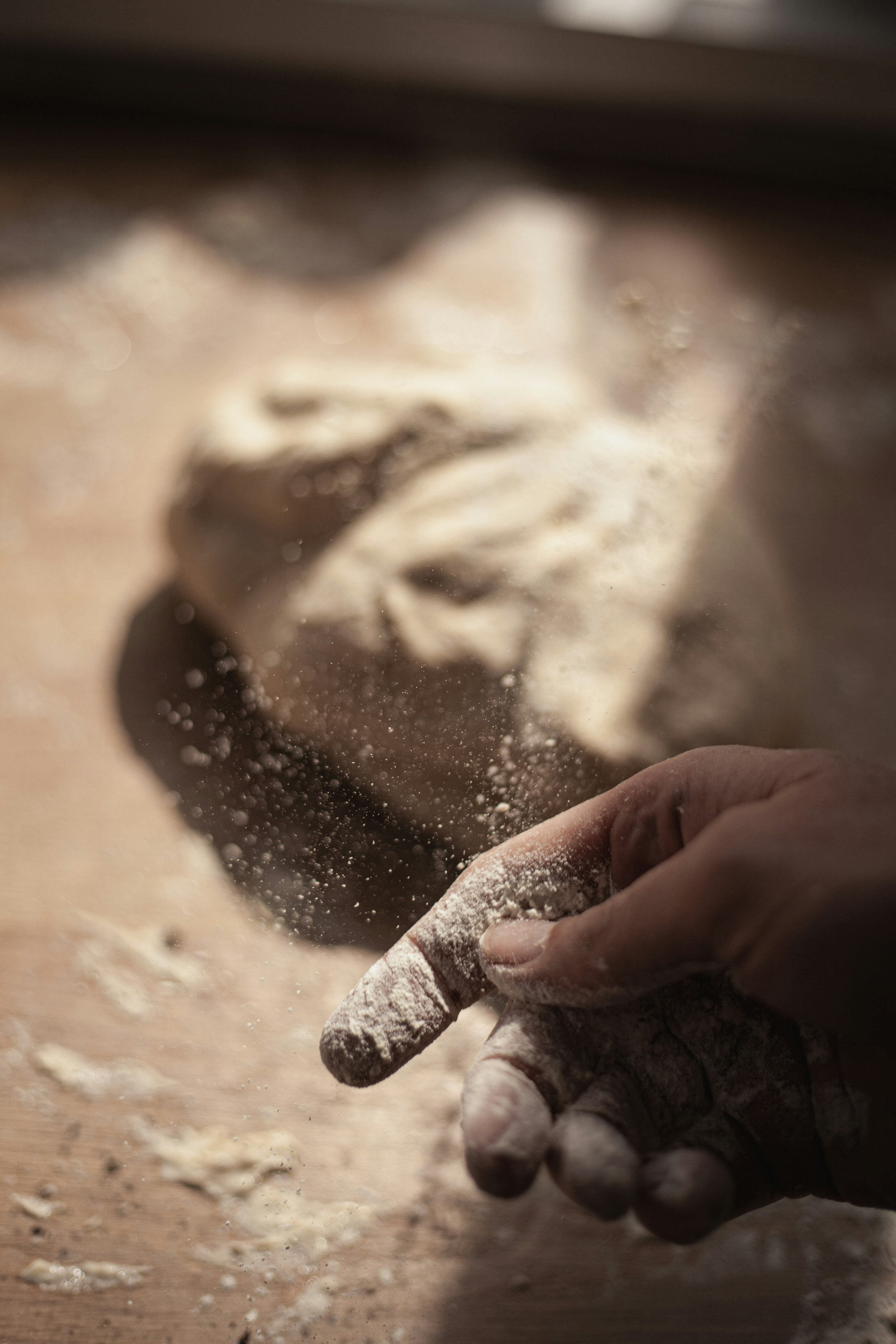 Mani che spolverano la farina sul piano di lavoro